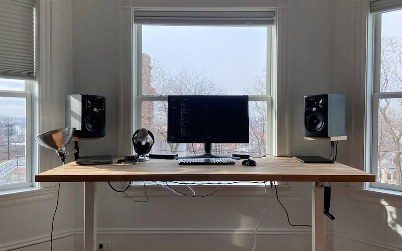 Mesa de madera con monitor, lámpara y ventana al fondo