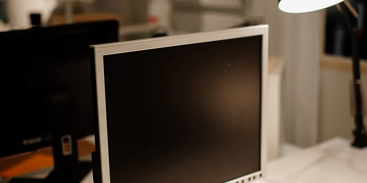 Monitor oscuro y lámpara de brazo sobre un escritorio blanco