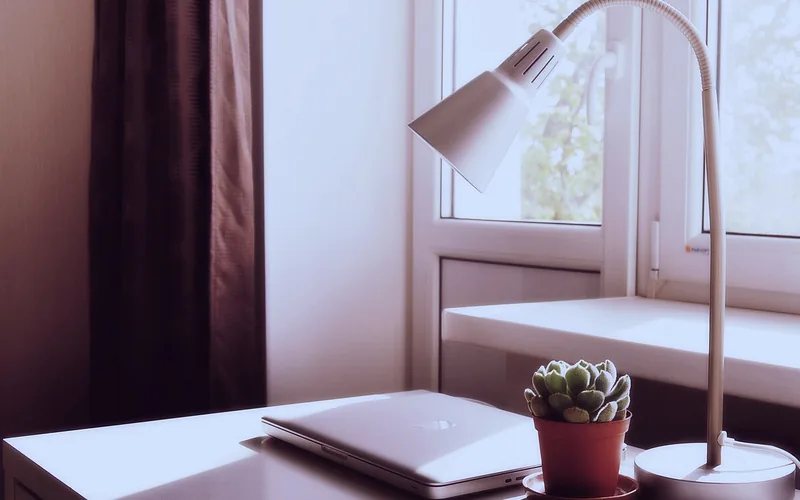 Lámpara de mesa junto a una ventana y un portátil cerrado